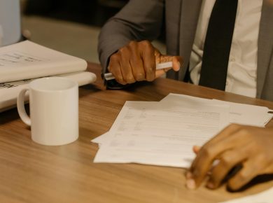 Free Close-up of a businessman holding and reviewing documents on a wooden desk. Stock Photo