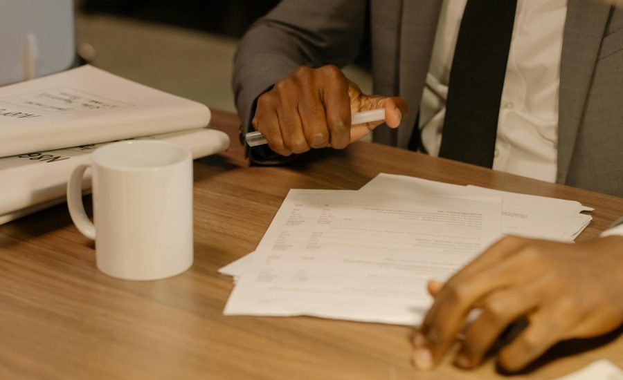 Free Close-up of a businessman holding and reviewing documents on a wooden desk. Stock Photo