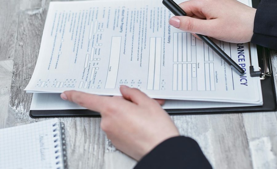 Free Close-up of hands analyzing insurance policy paperwork with pen on table. Stock Photo